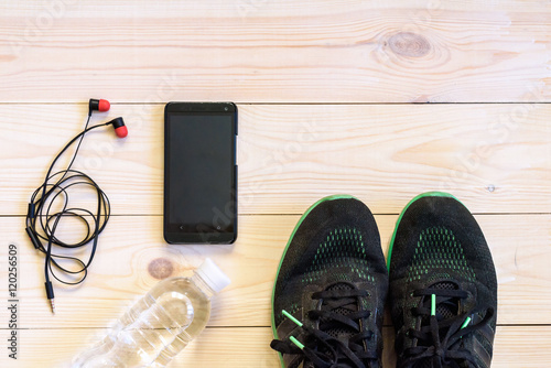 Flat lay shot of Sport equipment, shoes, water, earphone and phone on wooden background