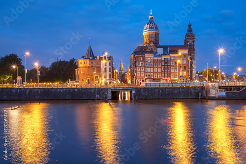 Night city view of Amsterdam canal and Basilica of Saint Nicholas, Schreierstoren or Weepers Tower and Oude Kerk, Holland, Netherlands.