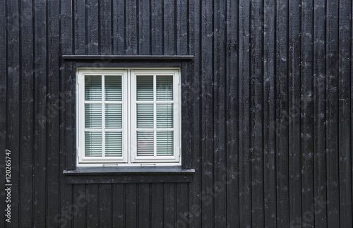 White casement window with mullions, and blinds on the inside, fastened in a black board and batten wood wall