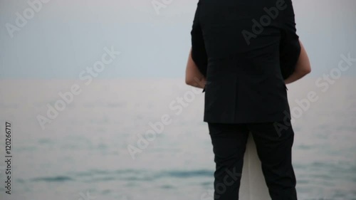 Sposo che abbraccia la sposa di dietro di fronte a un vuoto mare calmo photo