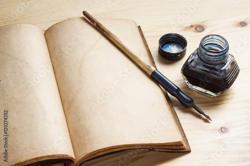 still life photography : quill pen with inkwell and opening old book on pine wood table photo