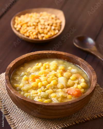 Vegetarian and vegan yellow split pea soup or stew with potato, carrot and celery in wooden bowl, photographed with natural light (Selective Focus, Focus in the middle of the soup)
