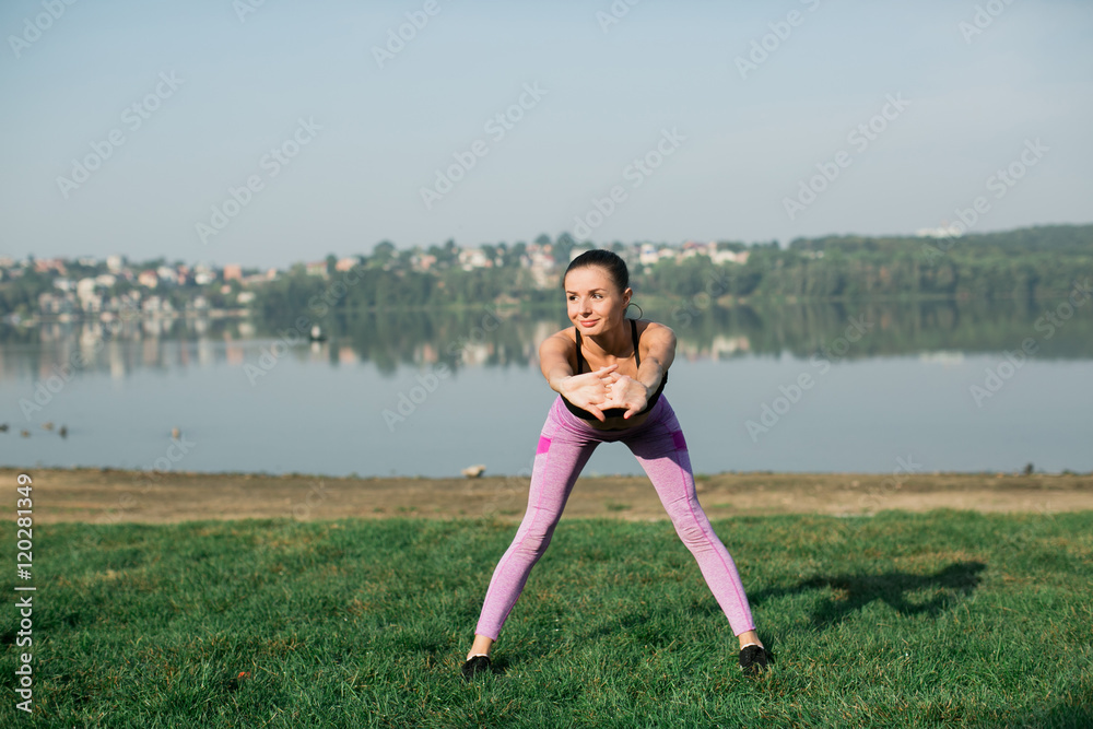 Young woman doing yoga in morning park near lake 
