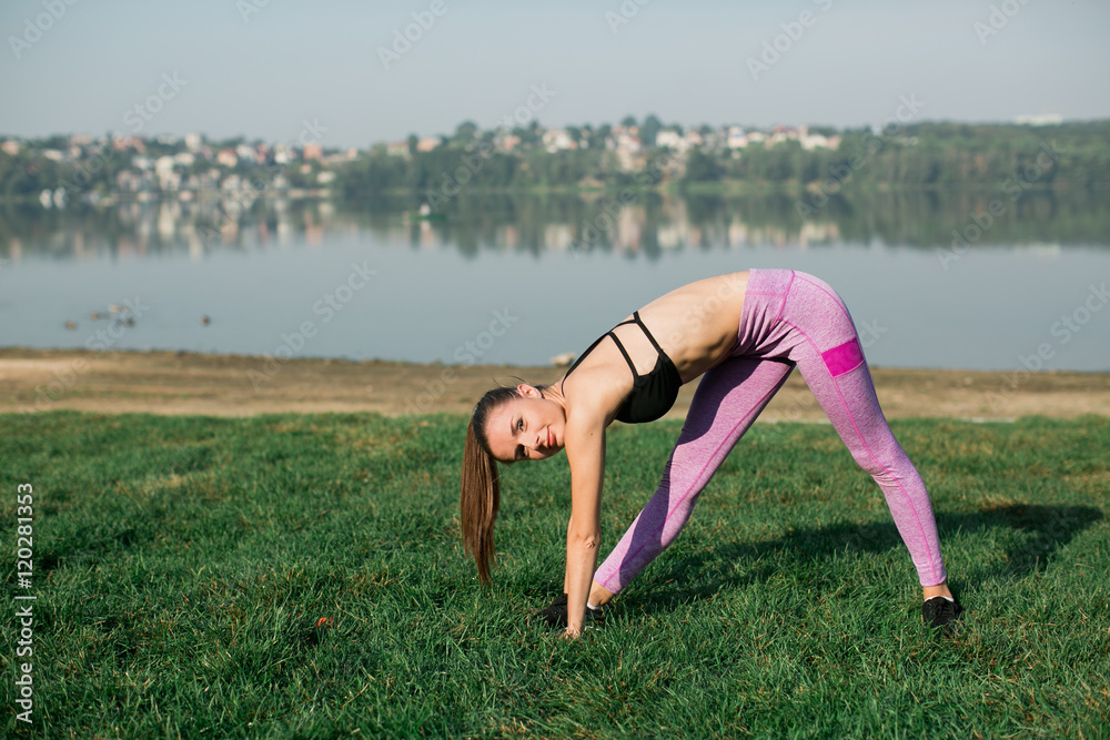 Fototapeta premium Young woman doing yoga in morning park near lake 