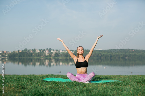 Young woman doing yoga in morning park near lake 