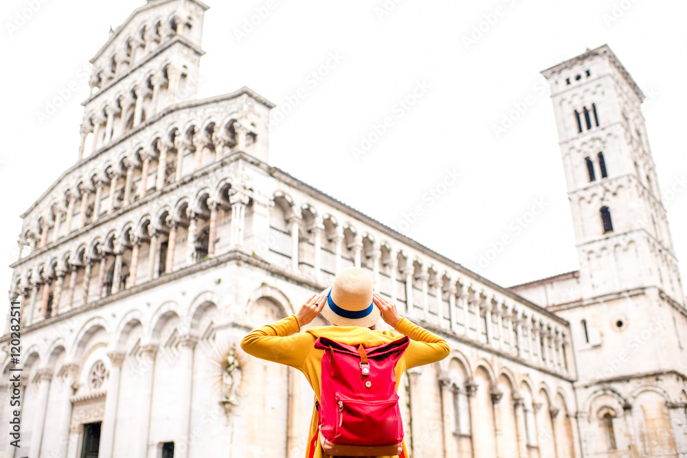 Young female traveler in yellow sweater and hat standing in front of San Michele basilica in Lucca old town in Italy. Having great vacations in Lucca. Back view