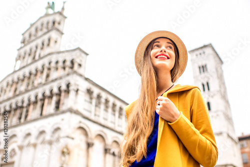 Young female traveler in yellow sweater and hat standing in front of San Michele basilica in Lucca old town in Italy. Having great vacations in Lucca