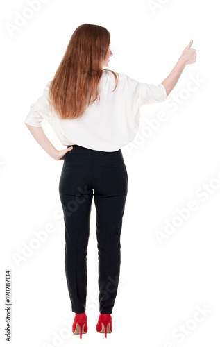 back view of standing young redhead business woman showing thumb up. beautiful businesswoman in black suit gesturing ok sign. Rear view people collection.  backside view of person.  Isolated over