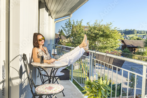 Young cute brunette woman sitting on a terrace and drinking a glass of wine in a sunny autumn afternoon