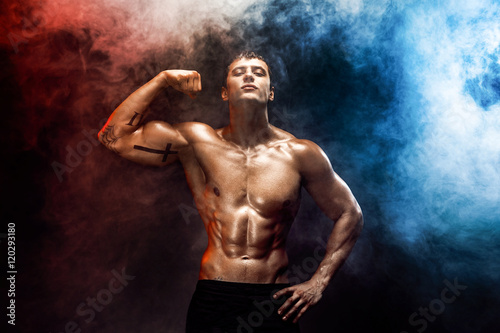 Portrait of muscular man posing at camera with shirtless body, misty smoky background © zamuruev