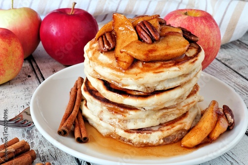 Autumn pancake stack with baked apples, pecans and cinnamon topped with maple syrup, table scene