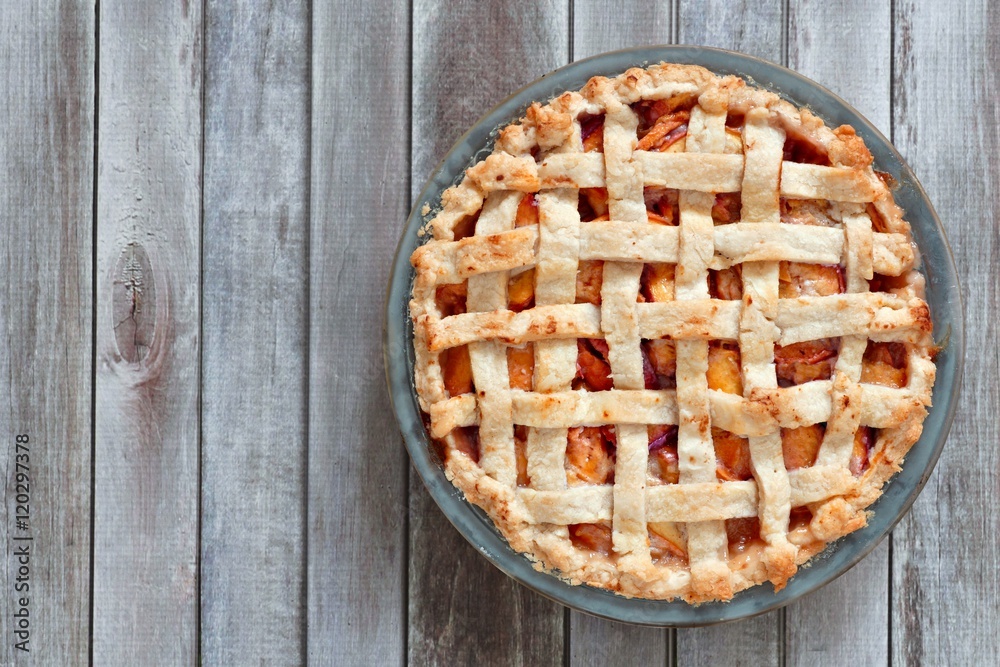 Rustic homemade peach pie in baking plate, above view on a wood background Rustic homemade peach pie in baking plate, above view on a wood background