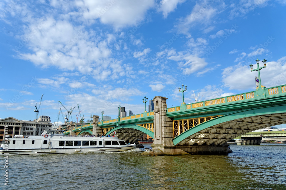 Fototapeta premium A cruise tourist boat passing under the Southwark bridge on the Thames river in London, UK.