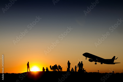 Group of people watching commercial airplane taking off during sunset on a mountain