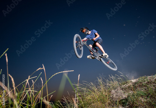 Male biker flying on a mountain bike against evening sky in the mountains. Cyclist is wearing sportswear helmet and glasses. Bottom view. Extreme cycling.