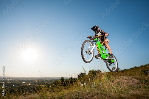 Bicyclist making high jump on a mountain bike from the slope into the distance against blue sky and small town