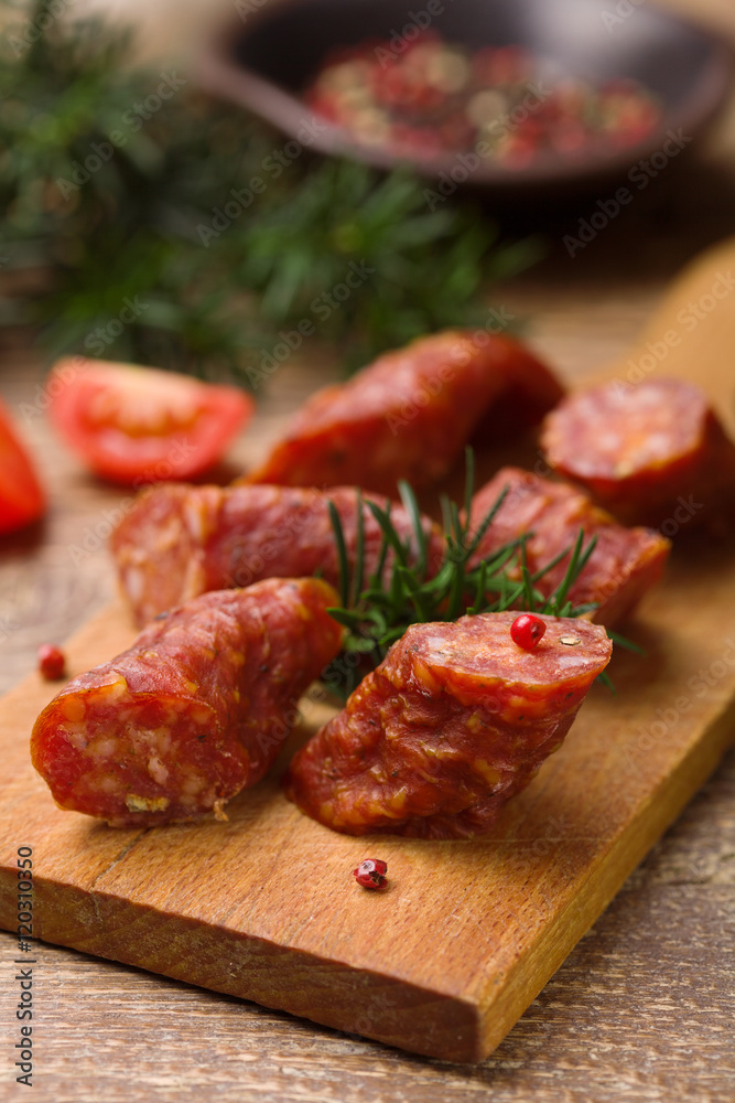 Delicious smoked sausage, sliced on a wooden board with spices.