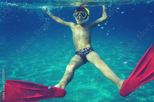Funny child diver with colorful diving accessories swimming underwater in sea. Summer vacation concept.
