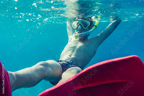 Funny child diver with colorful diving accessories swimming underwater in sea. Summer vacation concept.