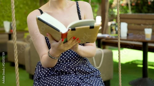 Girl sitting on the swing and reading a book while relaxing
 photo