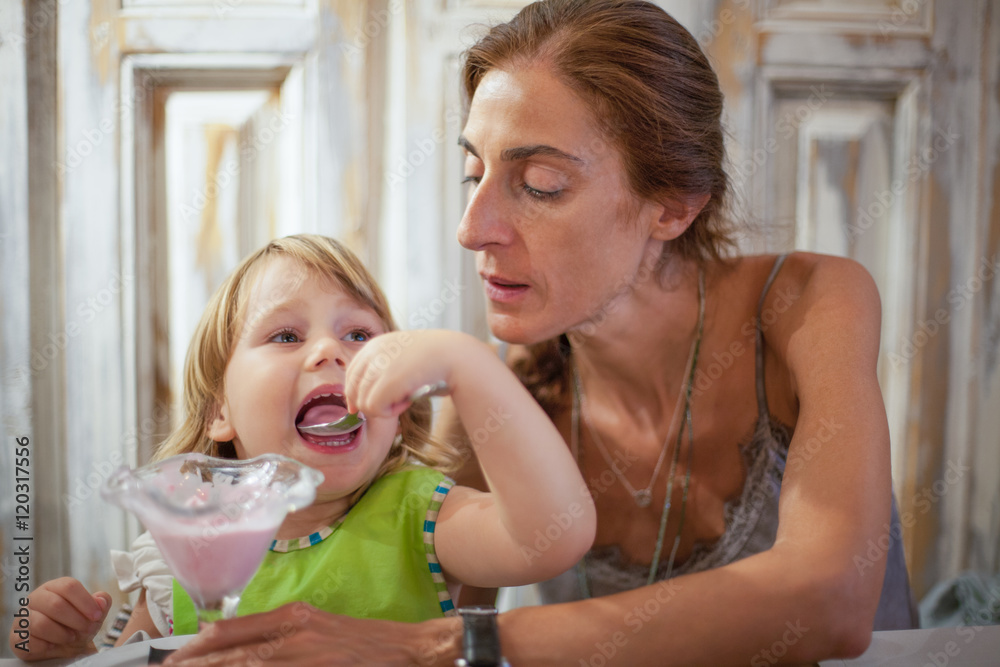 little child eating ice cream with mother at restaurant little child eating ice cream with mother at restaurant