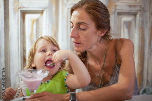 little child eating ice cream with mother at restaurant