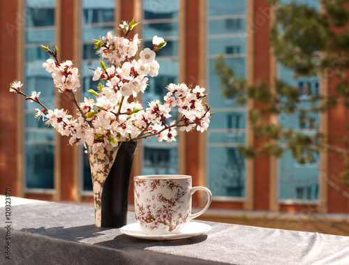 Чай в кружке под цветущими ветками дерева на балконе. На кружке рисунок веток дерева.