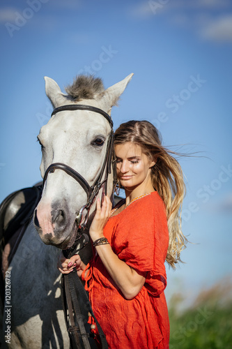 Portrait of young beautiful woman dressed in red tunic with horse in the meadow