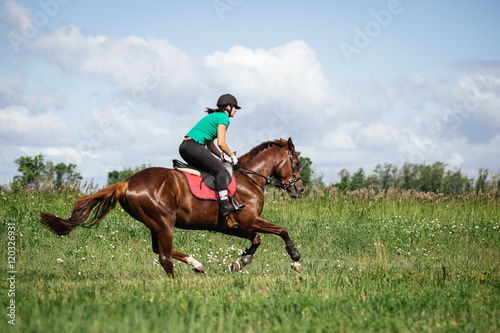 Young woman riding a horse on the green field