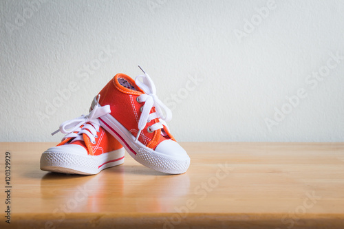 Baby sneakers on wooden table over wall grunge background, vintage style