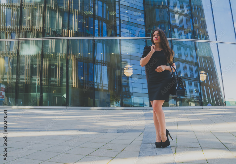 beautiful girl in black dress with purse and jacket in hand on the background of the business center beautiful girl in black dress with purse and jacket in hand on the background of the business center