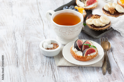 Bagels with different toppings - with cream cheese, figs, bananas, chocolate, blueberries for breakfast and a cup of tea on a rustic wooden table, selective focus