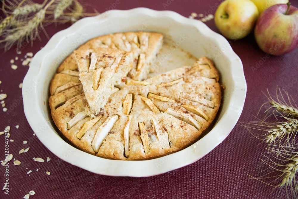 Homemade apple pie in the baking dish with apples and ears of wheat on the burgundy background Homemade apple pie in the baking dish with apples and ears of wheat on the burgundy background