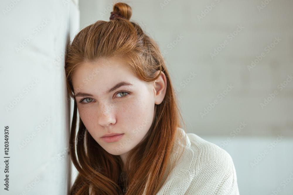 Closeup portrait of young adorable redhead woman wrapped in a white knitted blanket posing near white wall indoor natural light Closeup portrait of young adorable redhead woman wrapped in a white knitted blanket posing near white wall indoor natural light