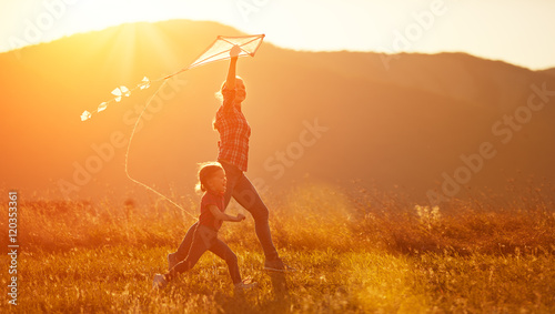 happy family mother and child run on meadow with a kite in summe