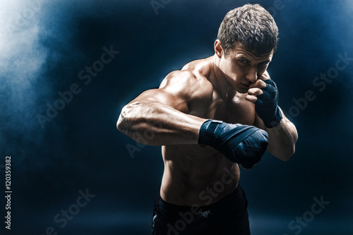 Fotografia Muscular kickbox or muay thai fighter punching in smoke.