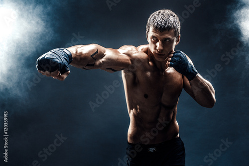 Muscular kick-box or muay thai fighter punching in smoke. © zamuruev
