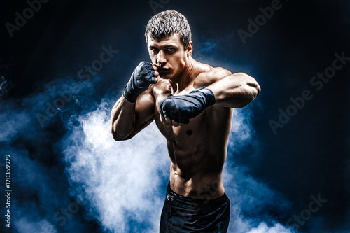 Obraz na płótnie Muscular kick-box or muay thai fighter punching in smoke.