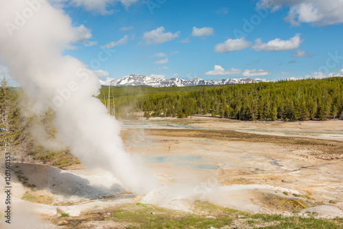Steamboat geyser in Norris Basin in Yellowstone National Park with hot steam, vapor, blue hot springs and mountains