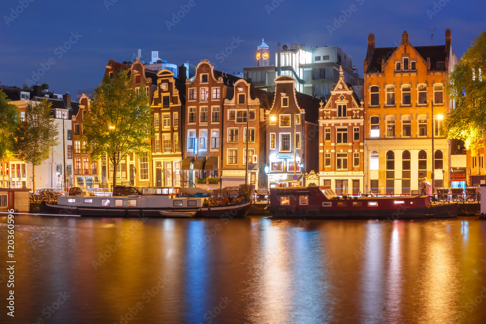 Fototapeta premium Amsterdam canal Amstel with typical dutch houses and houseboats with multi-colored reflections at night, Holland, Netherlands.