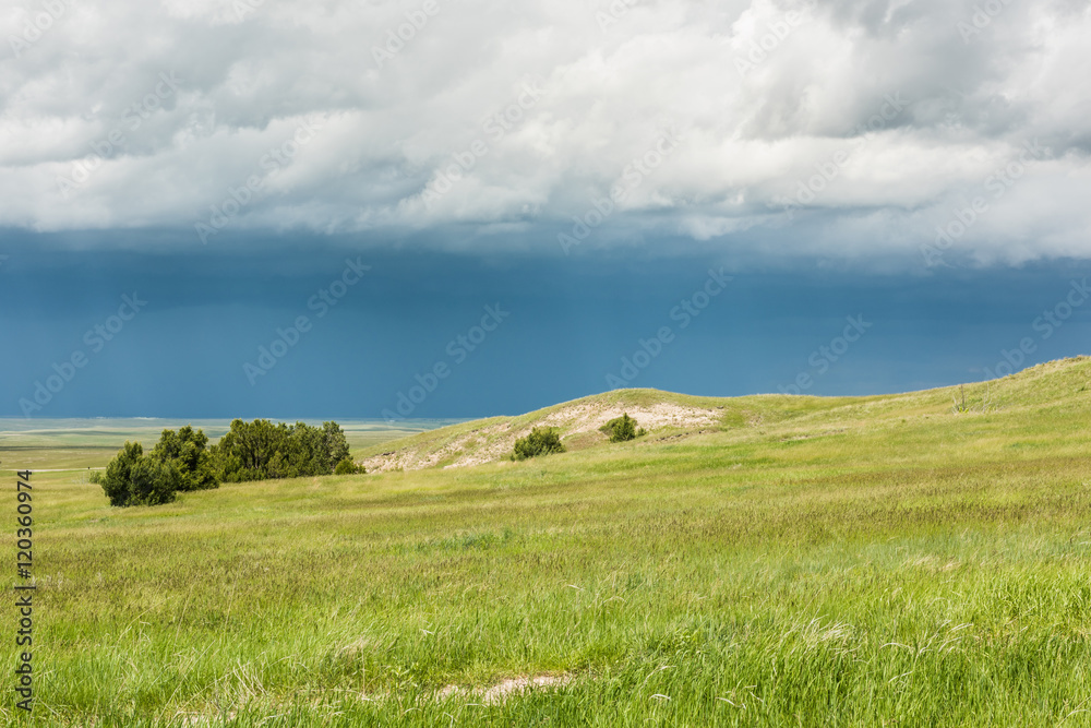Dark blue rain storm clouds contrast with green prairie steppe grass valley in Badlands National Park