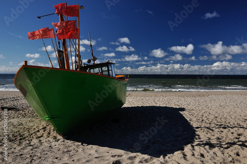 Zielony kuter rybacki stojący na piaszczystej plaży.