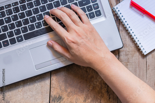 A man is working by using a laptop computer and financial documents on wooden table.