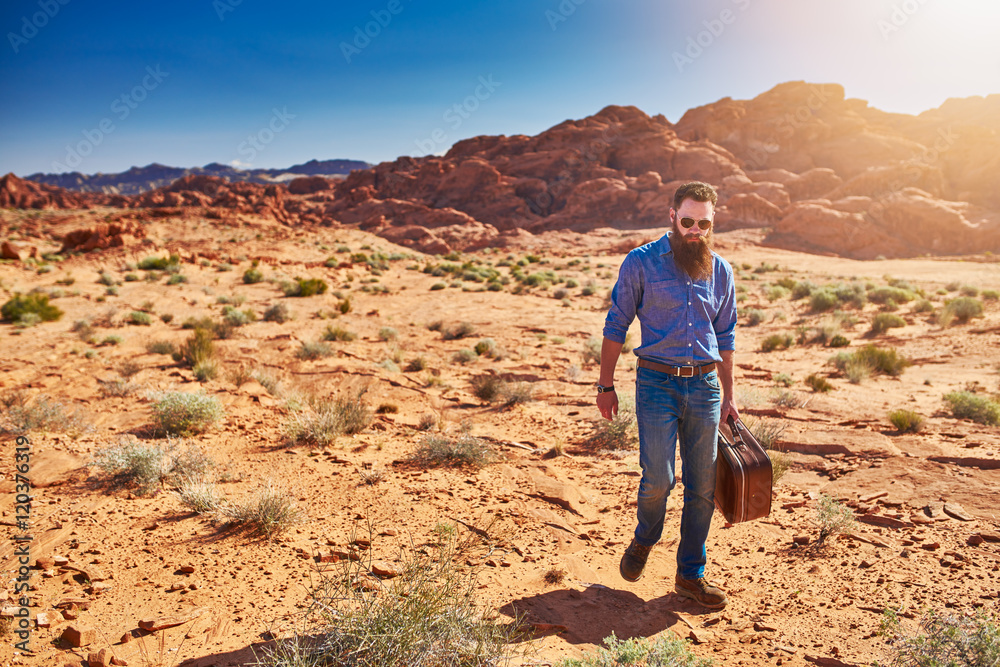 bearded man carrying stuicase through the desert in nevada
