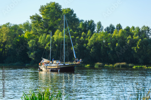 sailboat sailing on the river with deflated sails. Against the backdrop of the forest photo