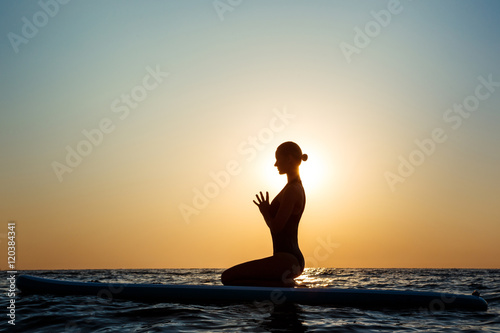 Photography Silhouette of beautiful girl practicing yoga on surfboard at sunrise