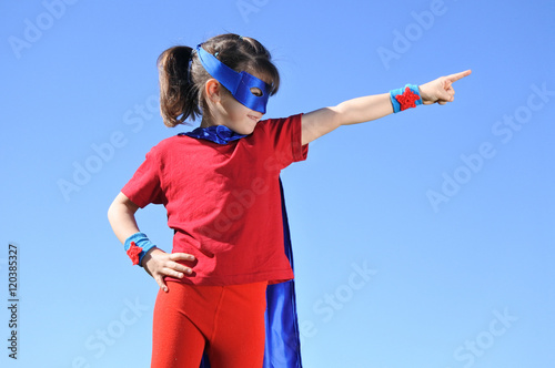 Obraz na płótnie Superhero girl points towards dramatic blue sky
