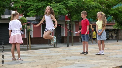 Smiling kids in school age playing together with jumping rope outdoors