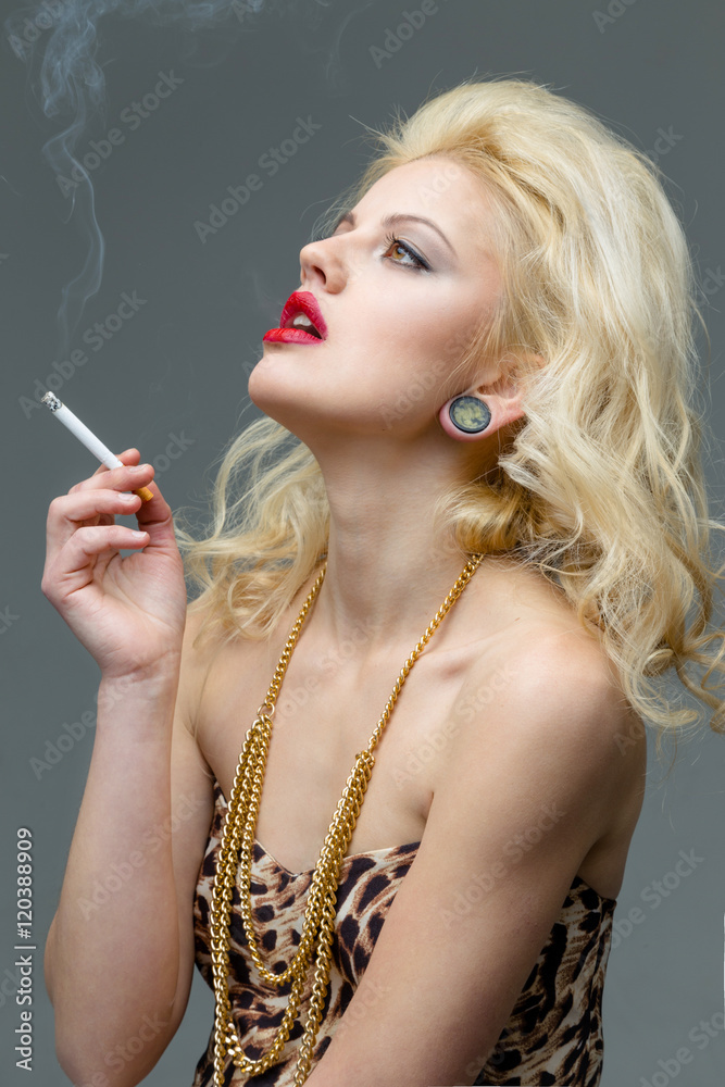Obraz premium Portrait of young beautiful blond woman with red lips in the studio in a beautiful dress smoking a cigarette