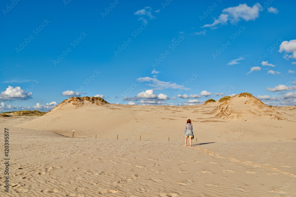 Young redhead woman walking under sun along endless sandy dunes